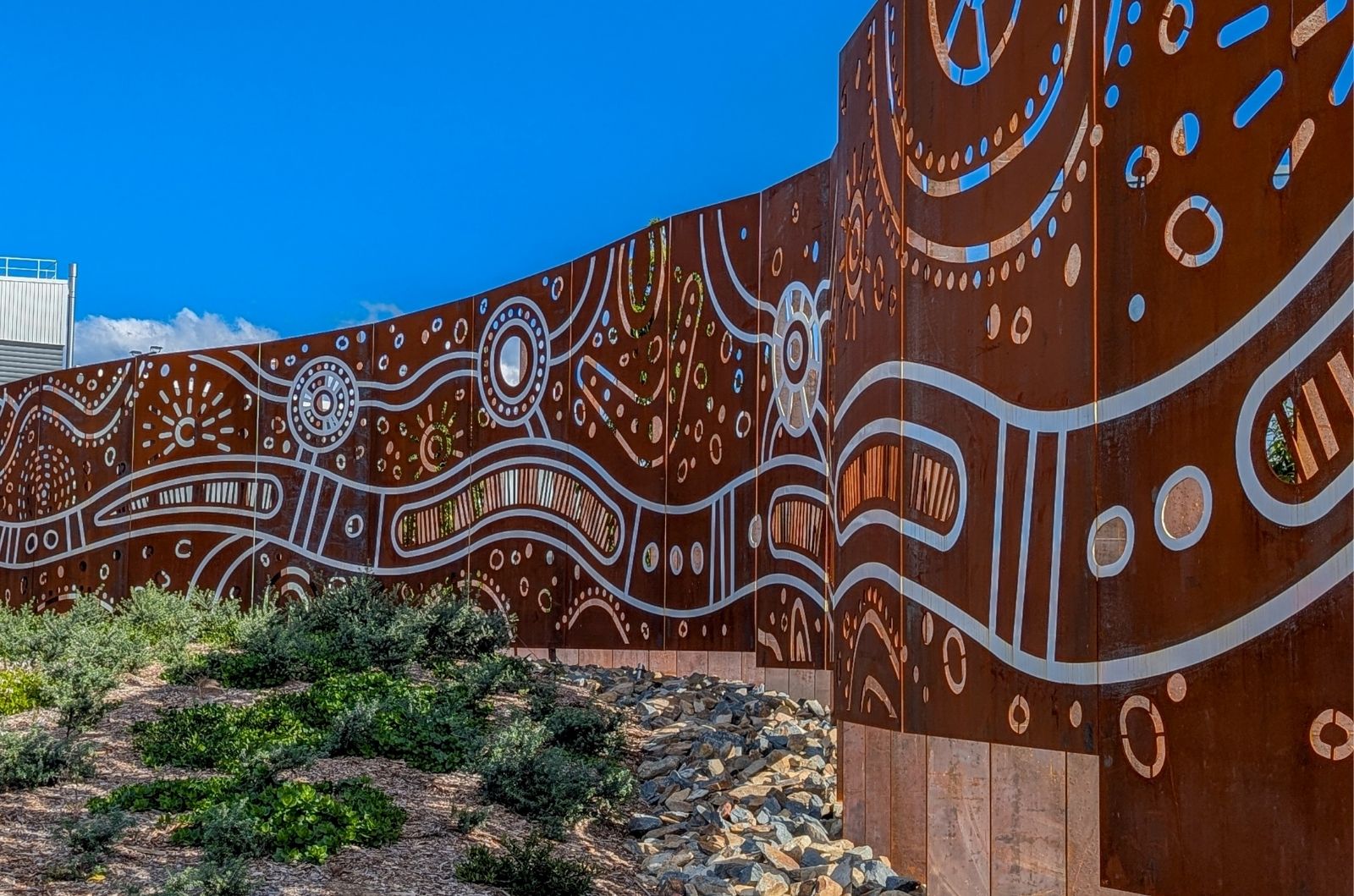 close view of multiple screen panels from a side angle on site demonstrating First Nations Artwork with surrounding landscapes showing greenery