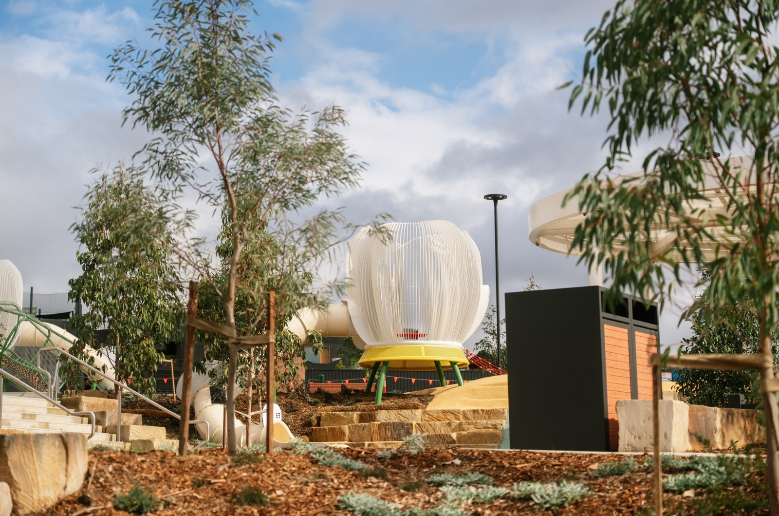 Image of The Gables Lake Foreshore park play equipment with planted trees, pathways and public rubbish disposal bin