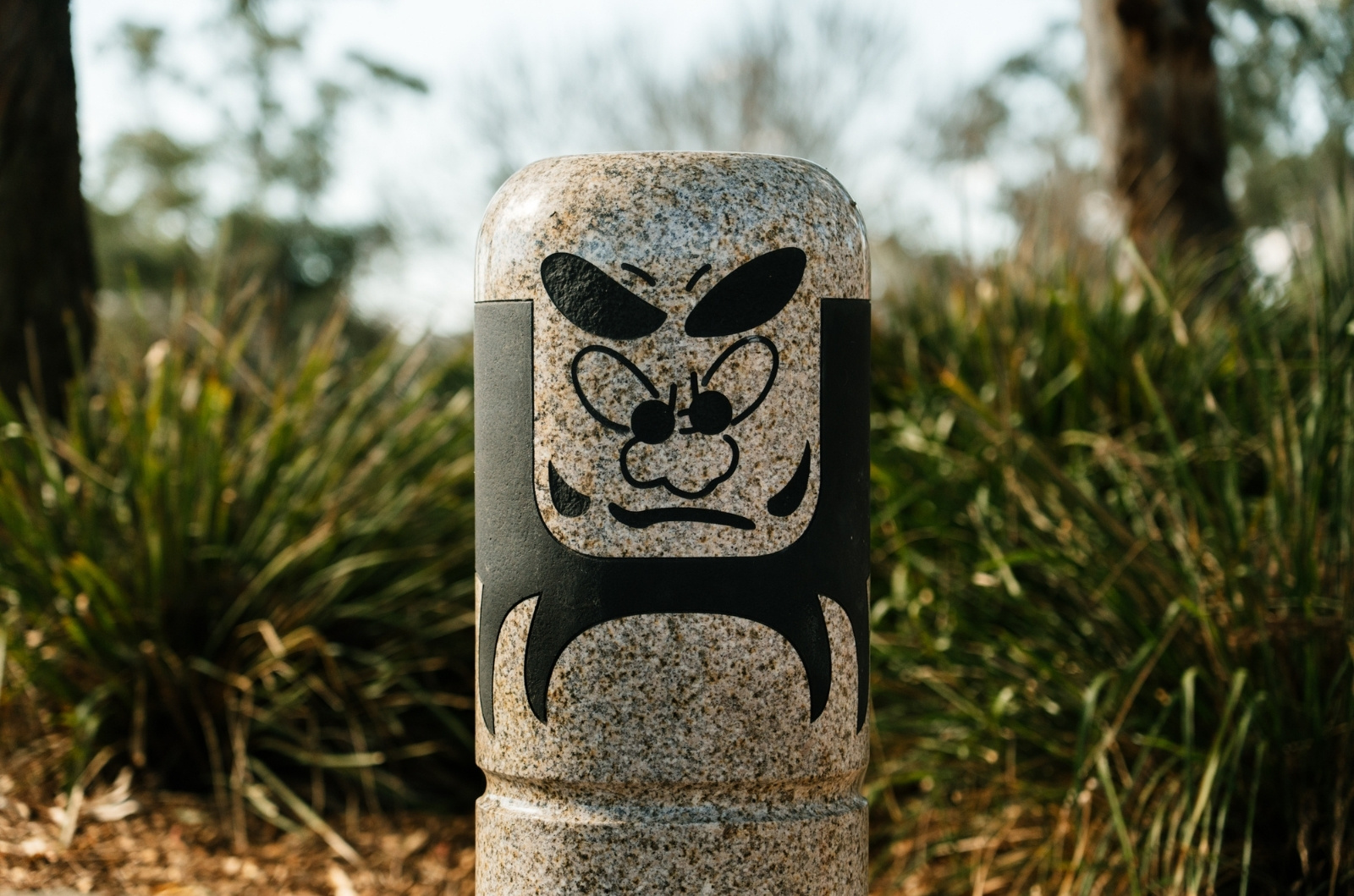 close up image of grey Daruma doll with green bushes in background