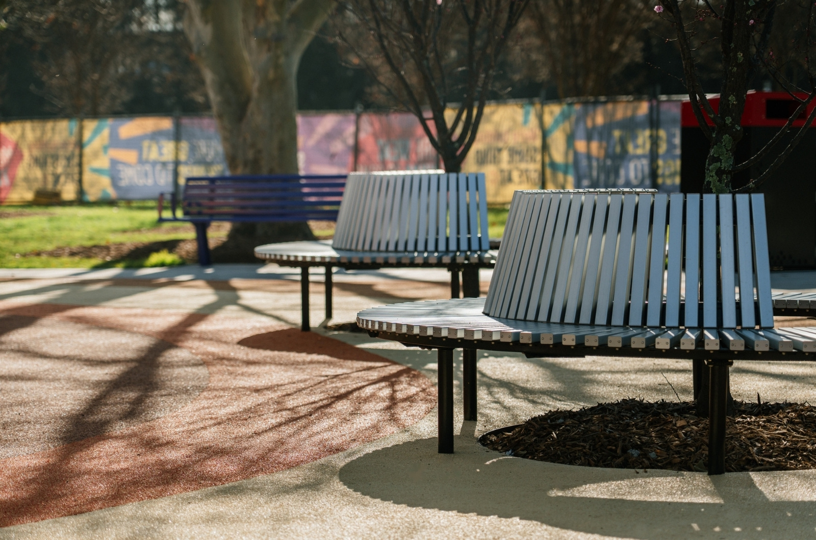 close up image of round steel benches that have trees in the centre of each bench, all underneath softball rubber